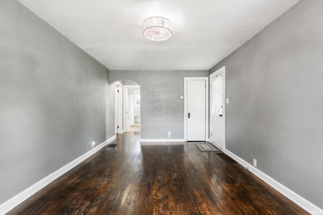 empty room featuring arched walkways, wood finished floors, and baseboards