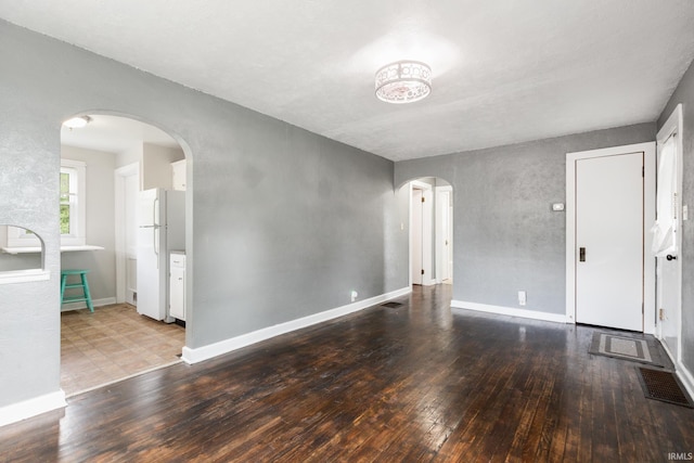 unfurnished living room featuring arched walkways, wood-type flooring, and baseboards