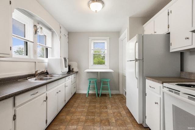 kitchen with white range with electric stovetop, dark countertops, stone finish floors, white cabinets, and baseboards