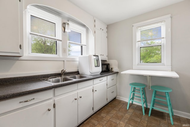 kitchen with a sink, dark countertops, stone finish flooring, and white cabinetry