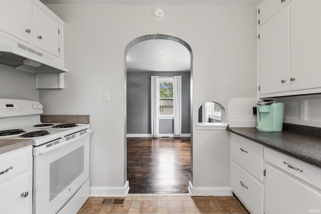 kitchen with electric stove, under cabinet range hood, arched walkways, and white cabinetry
