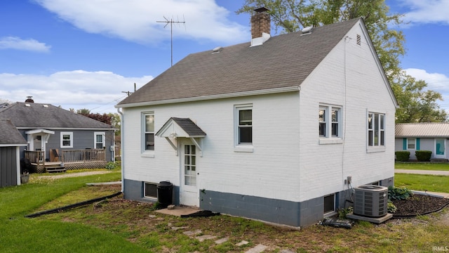 rear view of house with a chimney, cooling unit, a wooden deck, and a lawn