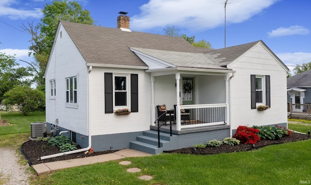 bungalow-style house with a chimney, cooling unit, a front lawn, covered porch, and a shingled roof