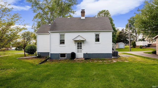 back of property featuring a chimney, a yard, a shingled roof, and cooling unit