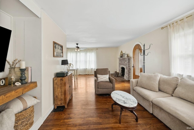 living area with wood finished floors, a ceiling fan, and a brick fireplace