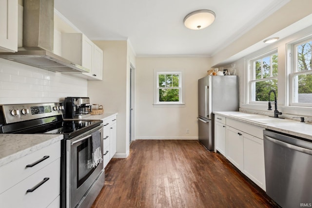 kitchen with appliances with stainless steel finishes, a sink, wall chimney range hood, ornamental molding, and dark wood finished floors