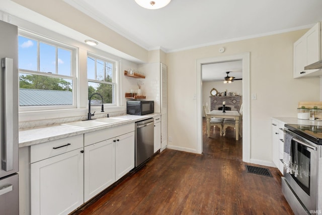 kitchen with appliances with stainless steel finishes, a sink, crown molding, dark wood finished floors, and baseboards