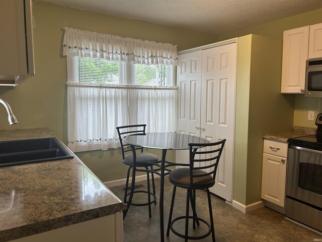 2705 Edgar St, Evansville, IN 47710 - kitchen with stainless steel appliances, a sink, white cabinets, baseboards, and dark countertops