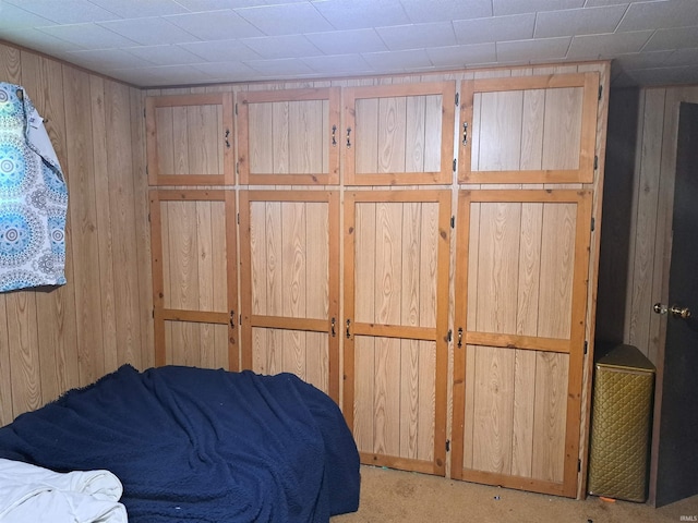 bedroom with wooden walls and light carpet