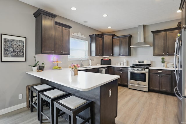 kitchen featuring appliances with stainless steel finishes, wall chimney exhaust hood, light wood-style floors, a peninsula, and dark brown cabinetry