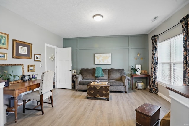 living area with light wood-type flooring, a decorative wall, a desk, and baseboards