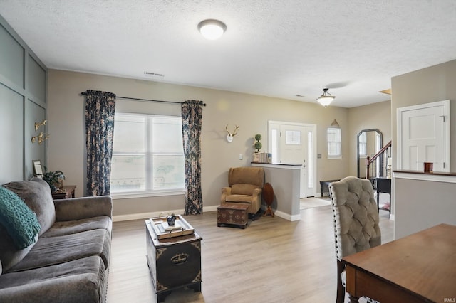 living room with light wood-type flooring, a textured ceiling, baseboards, and stairs
