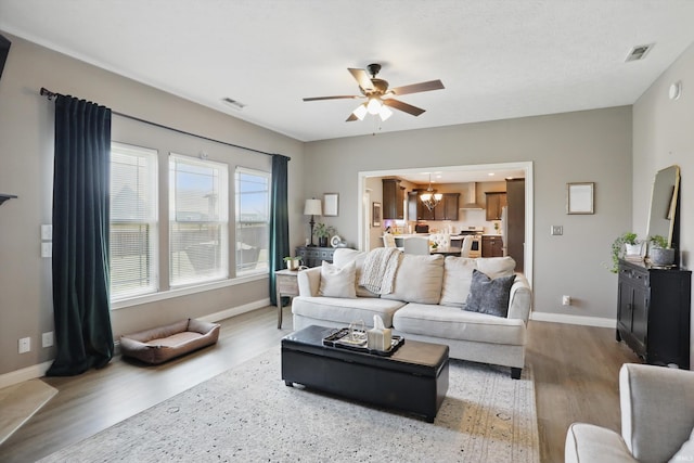 living room with wood finished floors, a ceiling fan, baseboards, and a chandelier