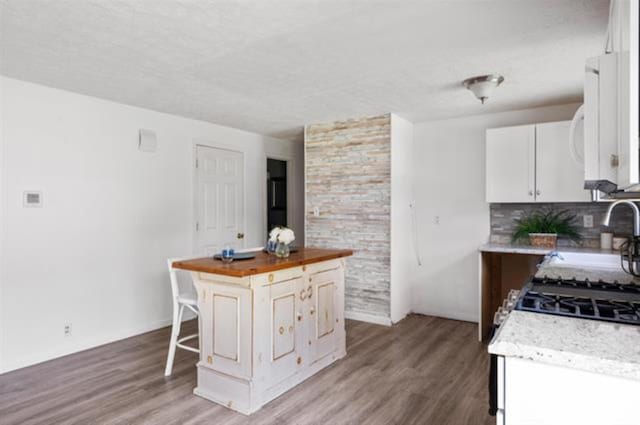 kitchen with light wood finished floors, white cabinets, butcher block countertops, a kitchen breakfast bar, and tasteful backsplash