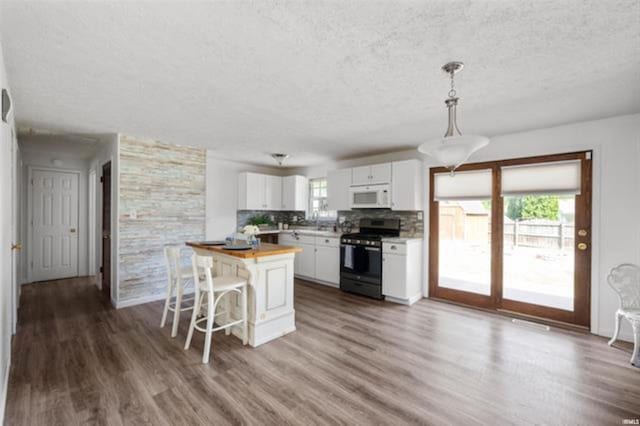 kitchen with stainless steel range, white microwave, butcher block counters, a textured ceiling, and a kitchen bar