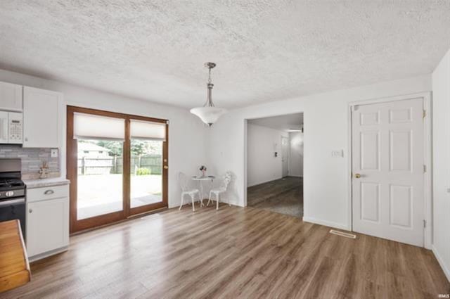 unfurnished dining area with light wood finished floors and a textured ceiling