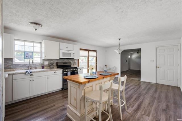 kitchen with gas range, white microwave, butcher block counters, a textured ceiling, and decorative backsplash