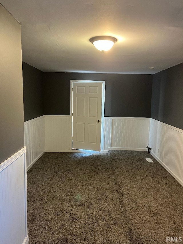 empty room featuring a wainscoted wall and dark colored carpet