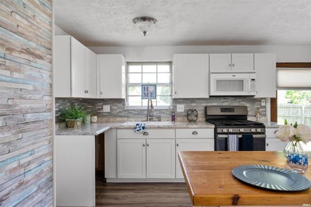 kitchen featuring white microwave, gas stove, a textured ceiling, light countertops, and white cabinets