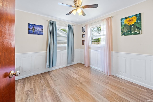 empty room featuring wood finished floors, a wainscoted wall, ceiling fan, crown molding, and a decorative wall