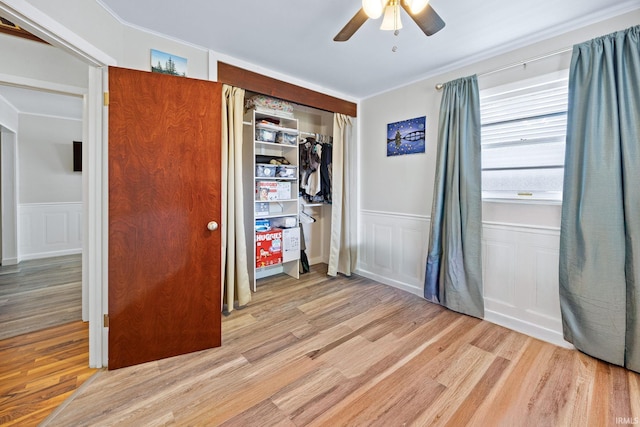 unfurnished bedroom with light wood-style floors, a wainscoted wall, a closet, a decorative wall, and a ceiling fan