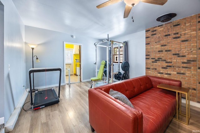 living room with wood finished floors, ceiling fan, baseboards, and brick wall