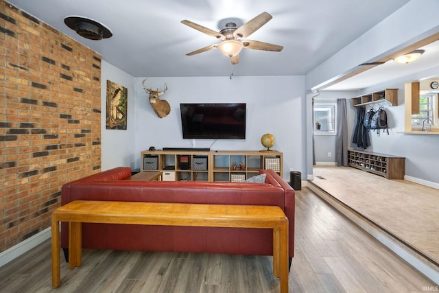 living area with a ceiling fan, wood finished floors, baseboards, and brick wall