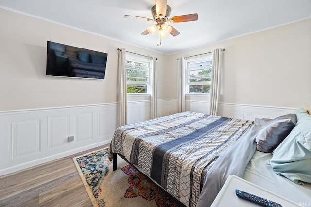 bedroom featuring a wainscoted wall, wood finished floors, ornamental molding, and a ceiling fan
