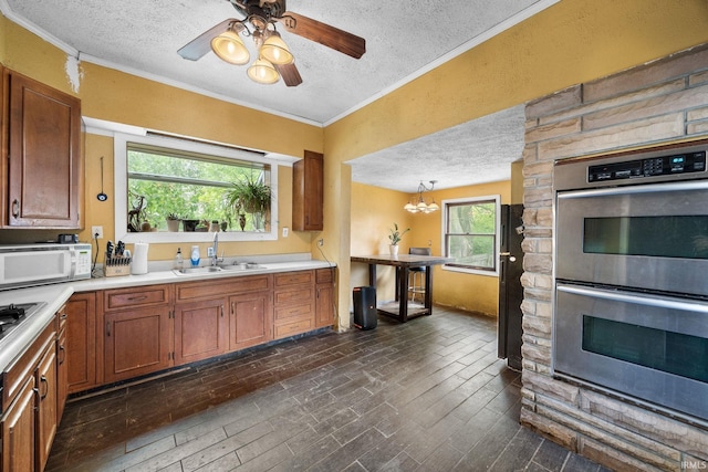 kitchen featuring a textured ceiling, white microwave, stainless steel double oven, a sink, and ornamental molding