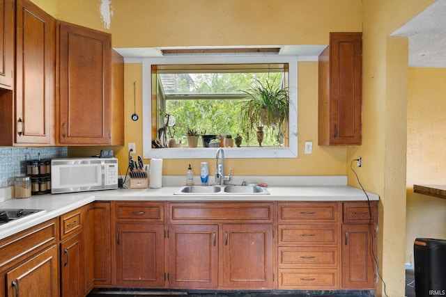 kitchen featuring white microwave, a sink, light countertops, and brown cabinets