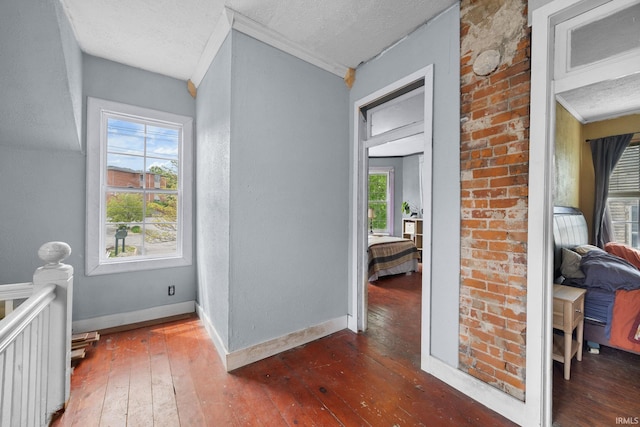 hallway featuring wood-type flooring, a textured ceiling, baseboards, and crown molding