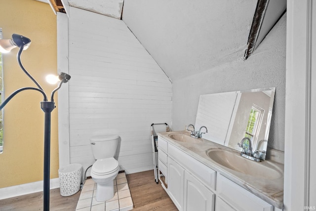 bathroom featuring wood finished floors, double vanity, toilet, and lofted ceiling