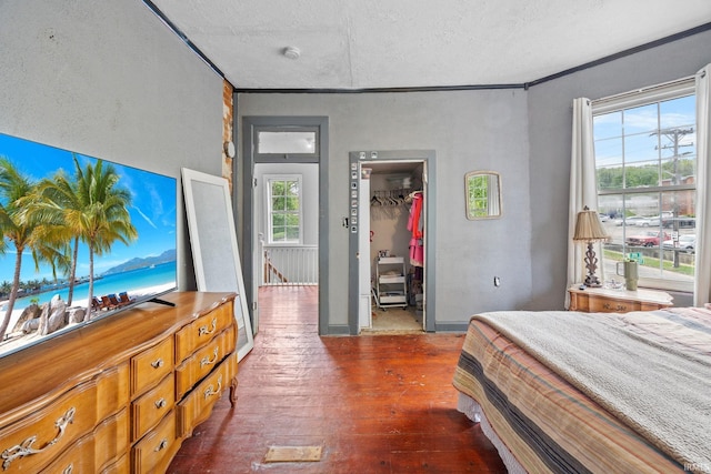 bedroom featuring dark wood-style flooring, a textured ceiling, a spacious closet, crown molding, and a closet