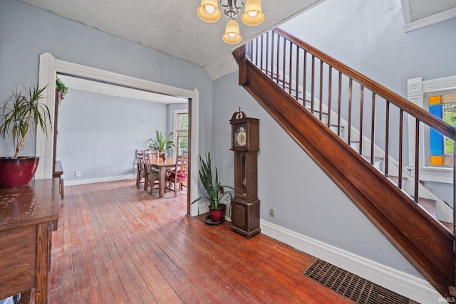 stairs with hardwood / wood-style flooring, baseboards, a chandelier, and vaulted ceiling