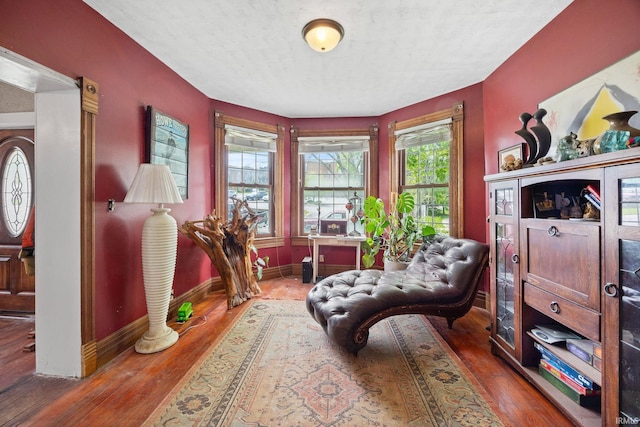 living area with baseboards, wood-type flooring, and a textured ceiling
