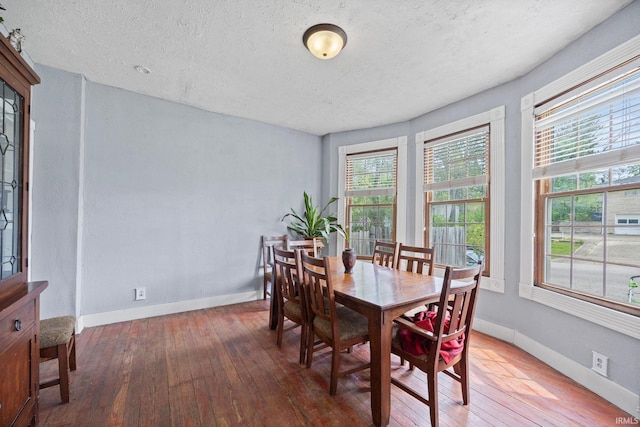dining space with wood-type flooring, a textured ceiling, and baseboards