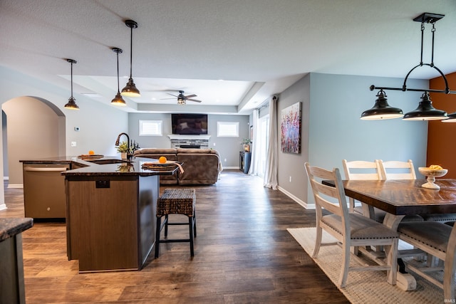 13865 Escondida Cv, Fort Wayne, IN 46845 - kitchen with a sink, ceiling fan, a raised ceiling, dark countertops, and an island with sink