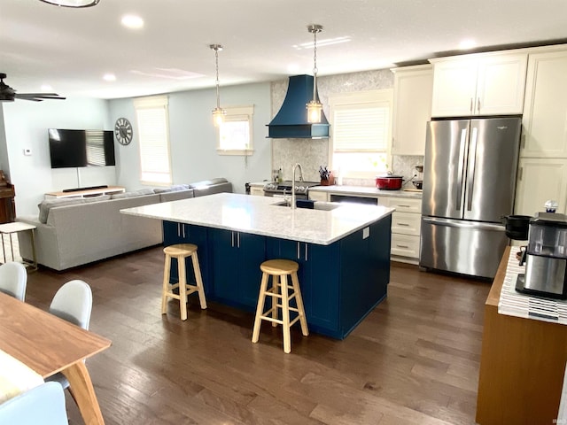 kitchen featuring freestanding refrigerator, premium range hood, a sink, a breakfast bar area, and dark wood-type flooring