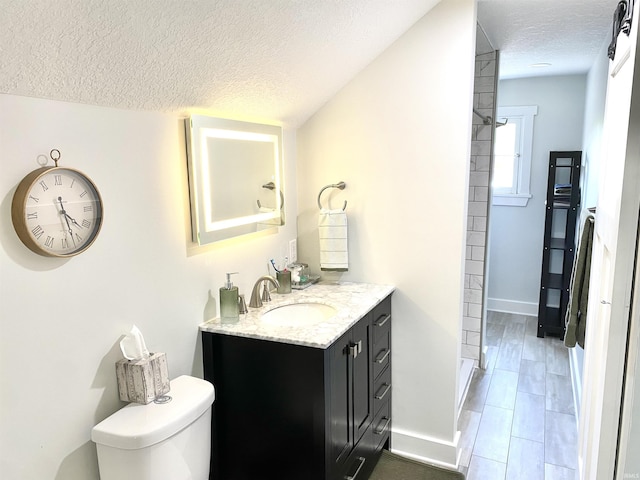 bathroom with a textured ceiling, baseboards, vanity, toilet, and vaulted ceiling