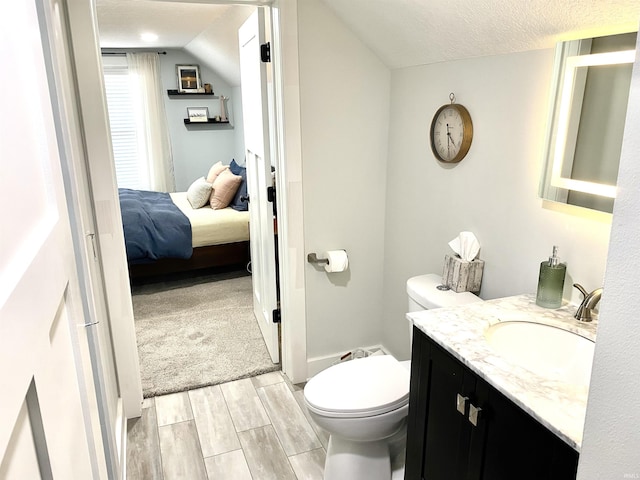 ensuite bathroom featuring toilet, wood finished floors, vanity, lofted ceiling, and a textured ceiling
