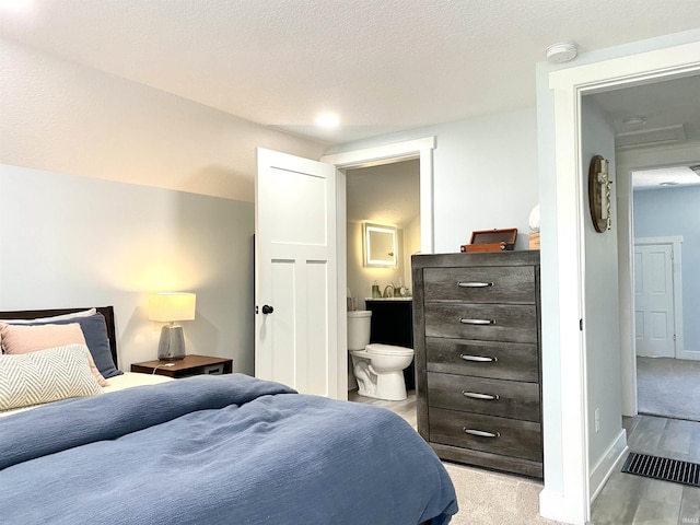 bedroom with baseboards, connected bathroom, and light wood-style flooring