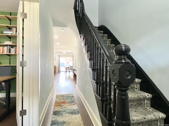 stairway featuring wood finished floors, arched walkways, and baseboards
