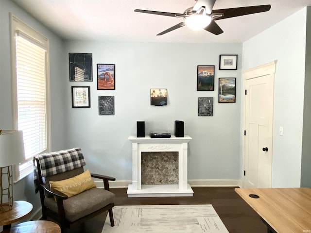 living area with a ceiling fan, baseboards, dark wood finished floors, and a fireplace with raised hearth