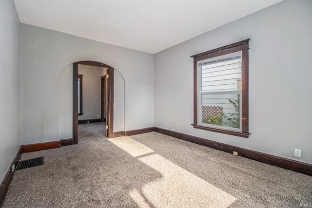 carpeted spare room featuring arched walkways and baseboards