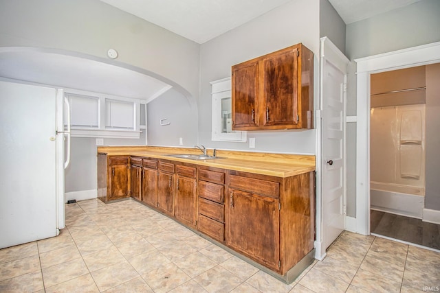 kitchen with freestanding refrigerator, a sink, arched walkways, and brown cabinets