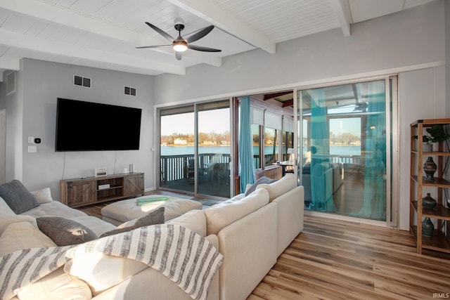 living area featuring light wood finished floors, ceiling fan, and beamed ceiling