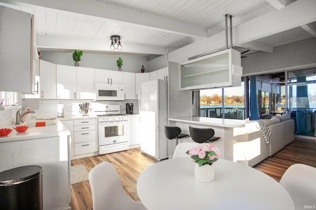 kitchen with white appliances, a sink, light wood finished floors, beam ceiling, and light countertops