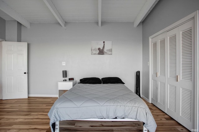 bedroom featuring beamed ceiling, wood finished floors, a closet, and baseboards