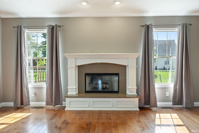 unfurnished living room with hardwood / wood-style floors, plenty of natural light, and a glass covered fireplace