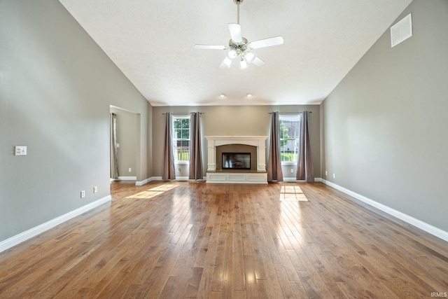 unfurnished living room featuring plenty of natural light, a ceiling fan, wood-type flooring, baseboards, and vaulted ceiling